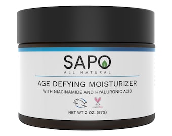 May include: A brown jar with a black lid labeled "SAPO ALL NATURAL AGE DEFYING MOISTURIZER WITH NIACINAMIDE AND HYALURONIC ACID" and a cruelty-free logo. The jar contains 2 ounces (57 grams) of moisturizer.