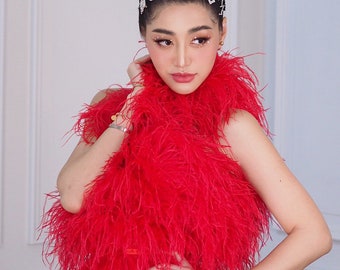 May include: A woman wearing a red feather dress with a high bun and multiple jeweled hair clips. The clips spell out "Boss" and "Lady".