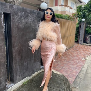 May include: A woman wearing a pink feather-trimmed top and a matching pink satin skirt with a side slit. She is wearing silver shoes and sunglasses.