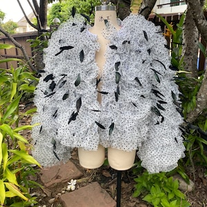May include: A white tulle jacket with black polka dots and black feathers. The jacket is on a white dress form.