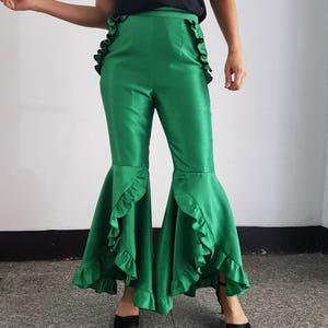 Peut inclure: Pantalon évasé vert avec une bordure de volants sur les côtés et le bas. Le pantalon est fait d'un tissu brillant.