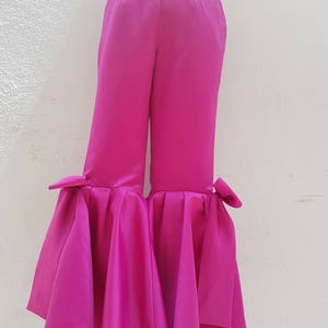Peut inclure: Pantalon large fuchsia &agrave; jambes larges avec un ourlet &agrave; volants et des d&eacute;tails en n&oelig;ud au bas de chaque jambe.