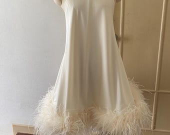 May include: A cream halter dress with a flared skirt and a trim of fluffy feathers at the hem. The dress is displayed on a mannequin, showcasing its elegant design and flowing silhouette. The dress is a formal wear item.