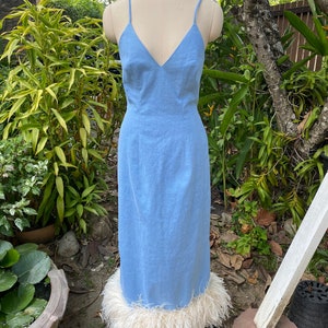May include: A light blue maxi dress with a V-neckline and a white feather trim at the hem.