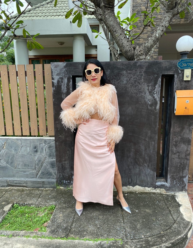 May include: A woman wearing a pink feather top and a matching pink skirt with a slit. She is wearing silver heels and sunglasses.