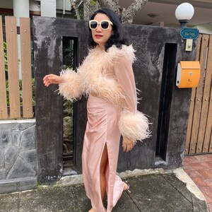 May include: A woman wearing a pink feather trim top and a matching pink satin skirt with a slit. She is wearing white sunglasses and silver heels.