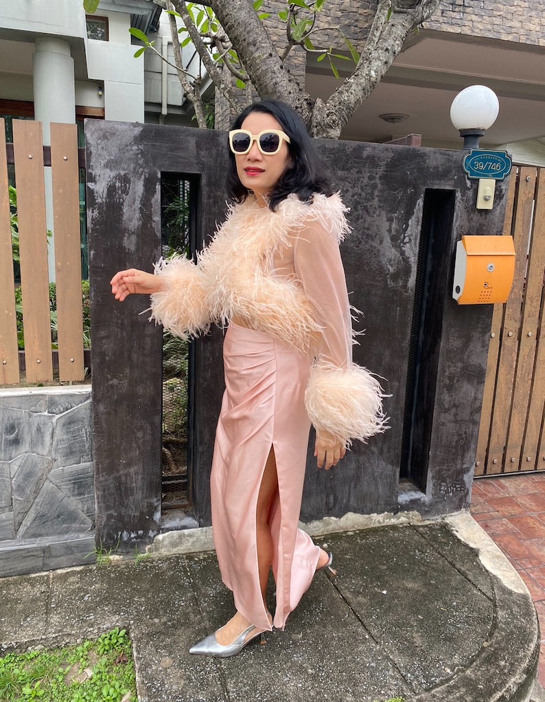 May include: A woman wearing a pink feather trim top and a matching pink satin skirt with a slit. She is wearing white sunglasses and silver heels.