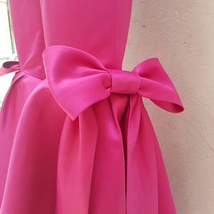 Peut inclure: Une robe rose bonbon avec un grand n&oelig;ud dans le dos.