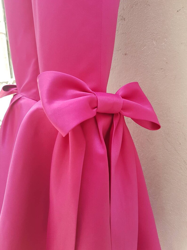 Peut inclure: Une robe rose bonbon avec un grand n&oelig;ud dans le dos.