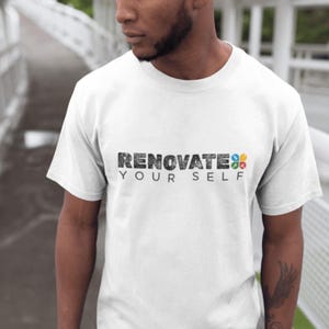 May include: White crew neck t-shirt with the text "RENOVATE YOUR SELF" in a distressed black font. The word "RENOVATE" is above "YOUR SELF". The word "SELF" has colorful squares. The shirt is short-sleeved.