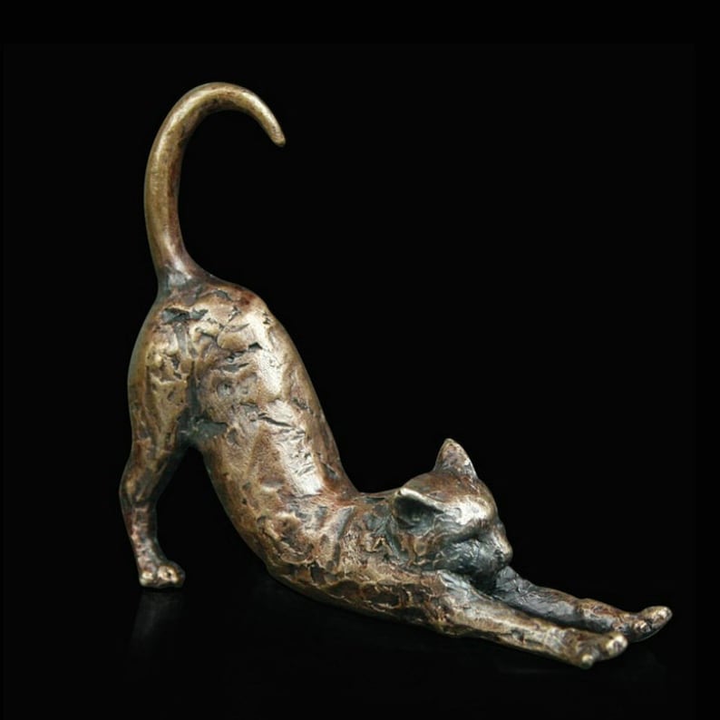 May include: A bronze sculpture of a cat stretching. The cat is in a yoga-like pose with its back arched and its tail curled over its head. The sculpture is detailed with textured fur and realistic features.
