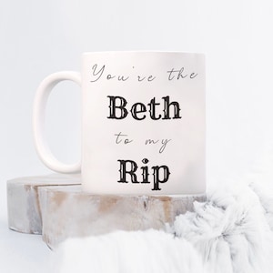 Op de afbeelding: Witte keramische mok met zwarte tekst die "You're the Beth to my Rip" zegt.