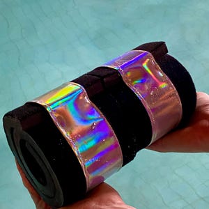 以下が含まれることがあります： 虹色のピンクとブルーのバンドが付いた黒いフォーム製のプールヌードル2本。ヌードルは人の手に持たれている