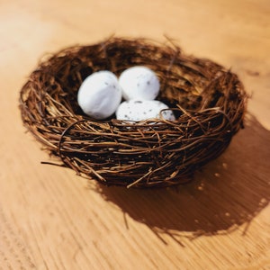 May include: A brown twig nest with three white speckled eggs inside.