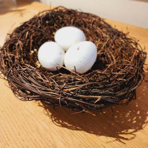 May include: Three white eggs in a brown woven bird's nest.