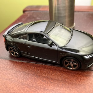 May include: A black die-cast model car with a glossy finish. The miniature vehicle features detailed wheels, a spoiler, and a sleek coupe design. The car is approximately 3 inches long.
