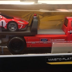 May include: A red toy Ford GT Heritage Edition car on a red toy flatbed tow truck. The tow truck has a Ford Performance logo and the number "1" on the side. The car is also numbered "1".