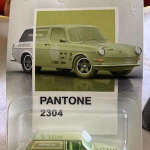 May include: A Hot Wheels Silver Series die-cast toy car in a blister pack. The vehicle is a light green station wagon featuring the text PANTONE 2304 on the side. The packaging displays the car illustration, the Hot Wheels logo, and the number 2/6.