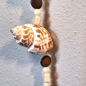 May include: A decorative seashell wind chime with brown and white seashells, wooden beads, and a gold bell at the bottom.
