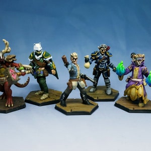 Op de afbeelding: Vijf beschilderde miniatuurfiguurtjes van fantasy-personages, elk staand op een zeshoekige basis. De personages omvatten een rode demon met hoorns, een elf gekleed in groen met een boog en pijl, een mens met een geweer, een elf gekleed in blauw met een zwaard en een katachtig wezen met gloeiende groene handen.