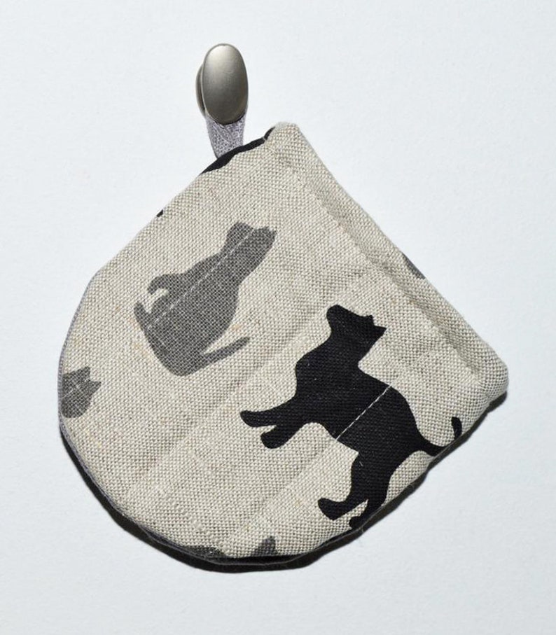 May include: A beige fabric pot holder with a black cat design. The pot holder has a silver hook.