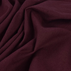 Puede incluir: Primer plano de una tela de color burdeos oscuro con una superficie lisa y ligeramente texturizada. La tela está doblada y drapeada, mostrando su naturaleza suave y fluida.