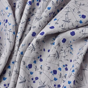 Puede incluir: Un primer plano de una tela de lino gris claro con un patr&oacute;n repetitivo de peque&ntilde;as flores azules y tallos grises. La tela est&aacute; doblada y drapeada, mostrando la textura y el detalle del dise&ntilde;o.