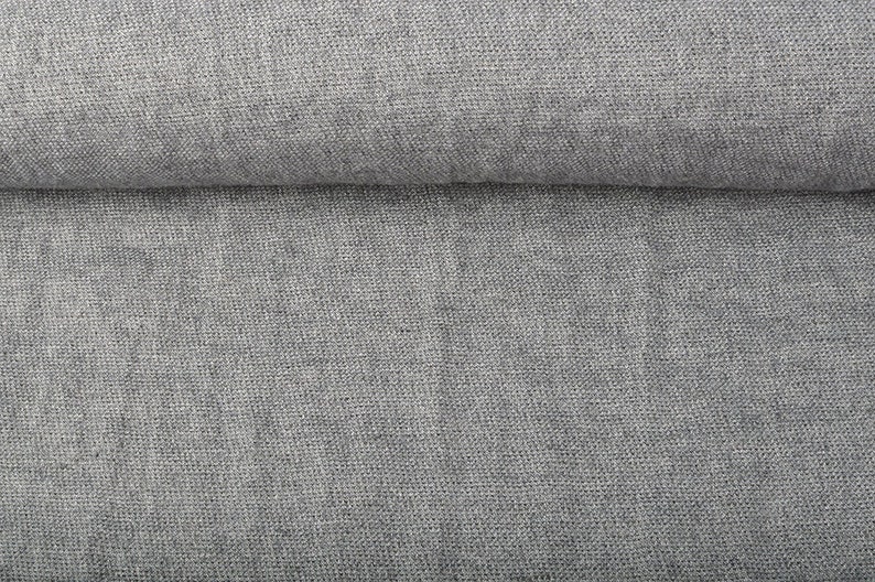 May include: Close-up of a folded, light gray linen fabric. The textile has a textured weave, with visible fibers creating a subtle, natural pattern. The fabric appears soft and pliable, suitable for clothing or home decor.