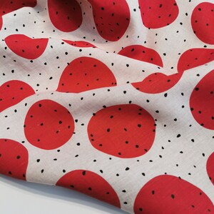 May include: Red and black fabric with a repeating pattern of large red circles with black dots inside. The background is a light beige color.