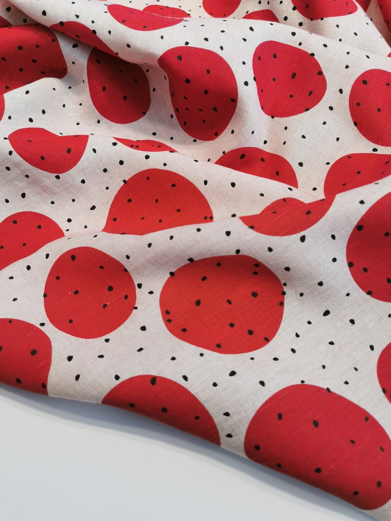 May include: Red and black fabric with a repeating pattern of large red circles with black dots inside. The background is a light beige color.