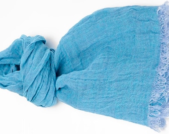 May include: A light blue scarf with a soft, textured appearance. The scarf is knotted and has a fringed edge. The fabric appears lightweight and suitable for warmer weather.