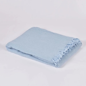 Könnte beinhalten: Eine hellblaue Tagesdecke mit strukturiertem Gewebe und Fransenrand.