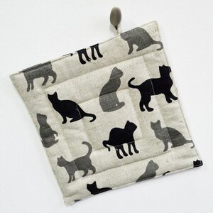 May include: A beige quilted pot holder with a black cat pattern. The pot holder has a loop for hanging.