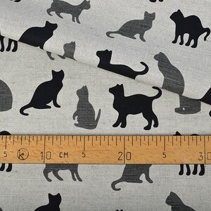 May include: A white fabric with a repeating pattern of black cat silhouettes. A ruler is placed on the fabric, showing measurements in inches and centimeters.
