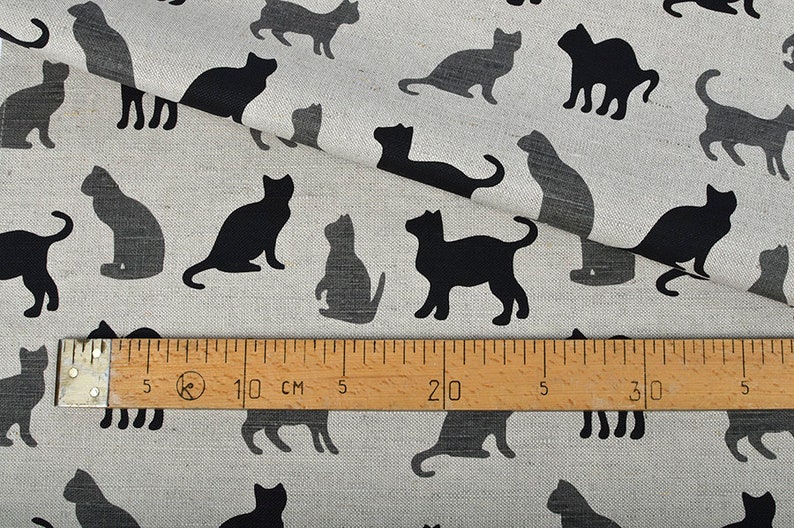 May include: A white fabric with a repeating pattern of black cat silhouettes. A ruler is placed on the fabric, showing measurements in inches and centimeters.