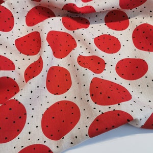 May include: Red and white fabric with a repeating pattern of red circles with black speckles. The fabric is folded and draped over a white surface.