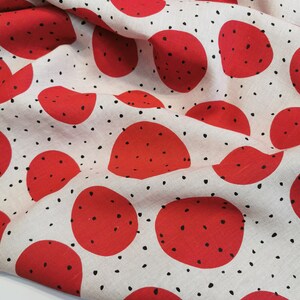 May include: Red fabric with a white background and a repeating pattern of red circles with black dots. The fabric is folded and has a textured surface.