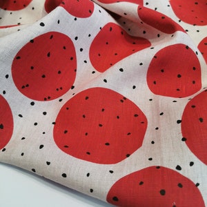 May include: Red and white fabric with a repeating pattern of large red circles with black dots. The fabric is folded and has a textured surface.