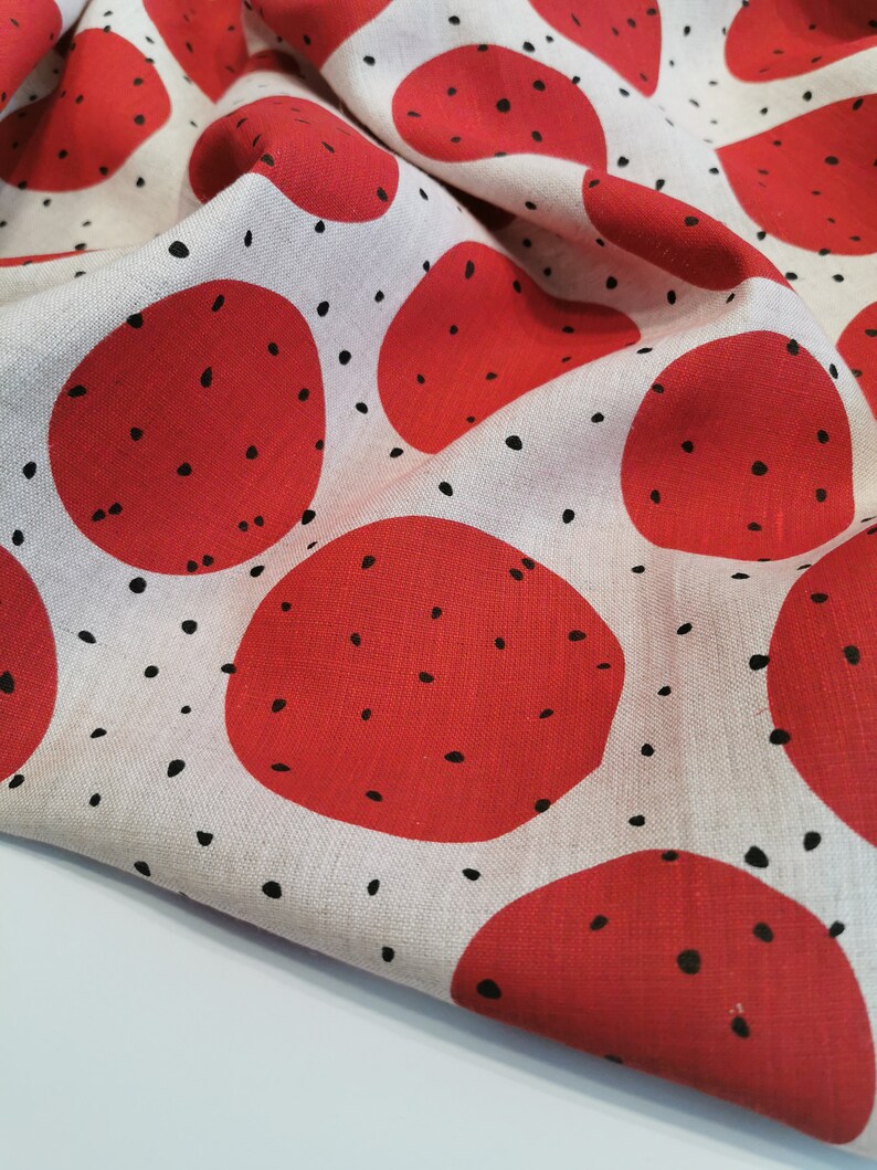 May include: Red and white fabric with a repeating pattern of large red circles with black dots. The fabric is folded and has a textured surface.