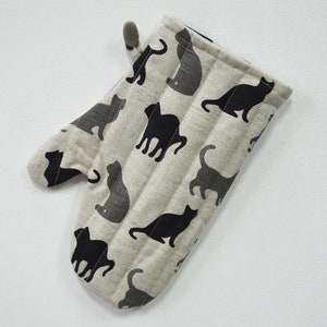 May include: A beige oven mitt with a black cat pattern. The mitt has a loop for hanging.