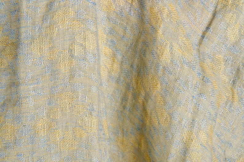 May include: A close-up of a textured fabric with a light blue and yellow pattern. The fabric has a woven appearance and is slightly wrinkled.