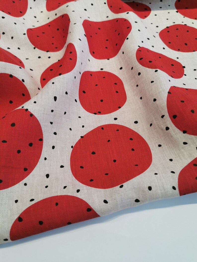 May include: Red and white fabric with a repeating pattern of red circles with black dots. The fabric is folded in half.