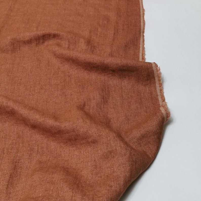 Puede incluir: Primer plano de una tela de lino de color &oacute;xido con una superficie ligeramente texturizada. La tela est&aacute; doblada y drapeada, mostrando sus arrugas y pliegues naturales.