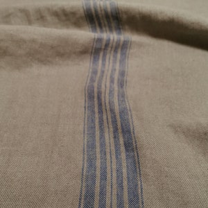 K&ouml;nnte beinhalten: Nahaufnahme eines beigefarbenen Stoffes mit einem vertikalen Streifen aus blauen und wei&szlig;en Streifen.