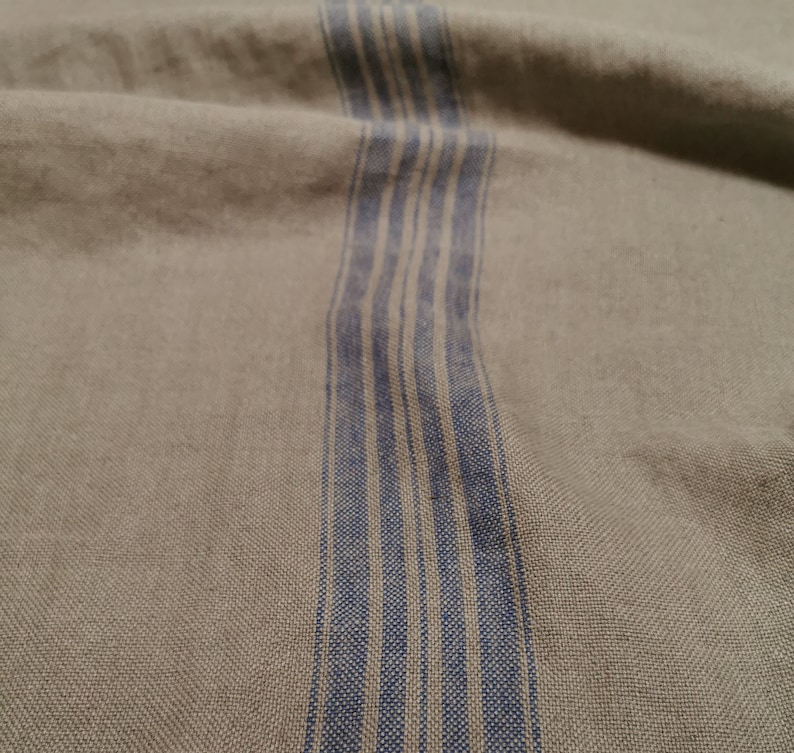K&ouml;nnte beinhalten: Nahaufnahme eines beigefarbenen Stoffes mit einem vertikalen Streifen aus blauen und wei&szlig;en Streifen.