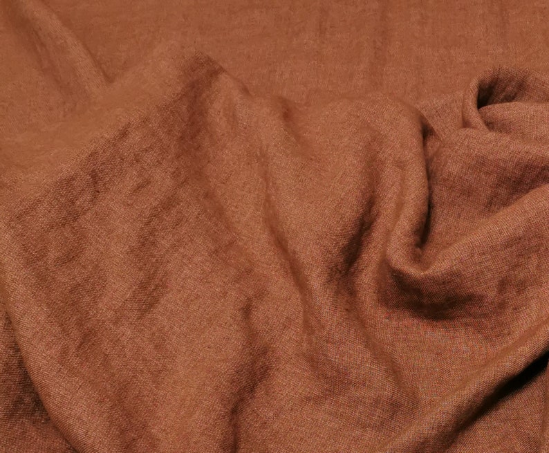 Puede incluir: Primer plano de una tela de color &oacute;xido con una textura tejida. La tela est&aacute; doblada y drapeada, mostrando su textura suave y fluida.