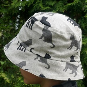 May include: A white bucket hat with a black cat print. The hat is made of a soft, lightweight fabric and has a wide brim.
