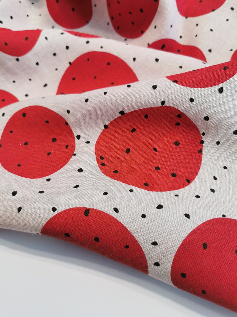 May include: White fabric with a repeating pattern of red circles with black dots. The fabric is folded and the circles are overlapping.