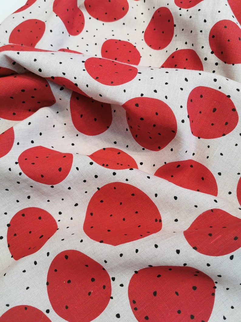 May include: White fabric with a repeating pattern of red circles with black speckles. The fabric is wrinkled and folded.