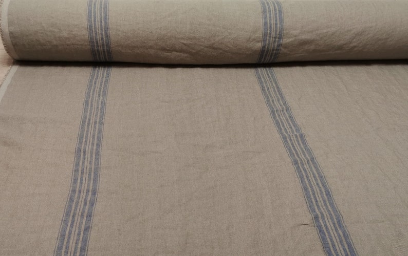 K&ouml;nnte beinhalten: Eine Rolle aus nat&uuml;rlichem Leinenstoff mit blauen Streifen. Der Stoff hat eine rustikale, strukturierte Optik und Haptik.